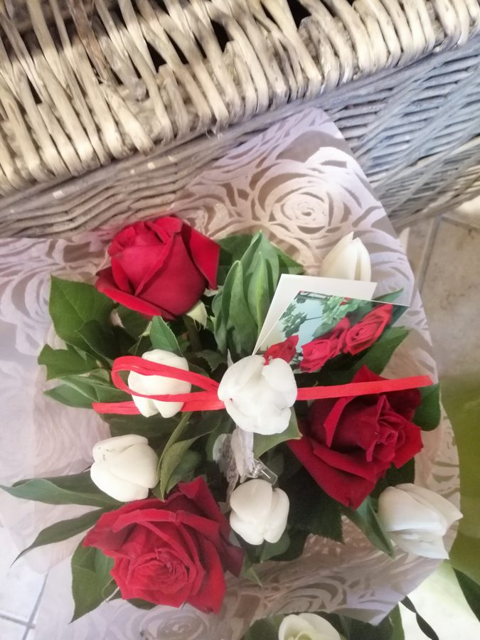 Sarkano rožu un balto tulpju pušķis iepakojumā